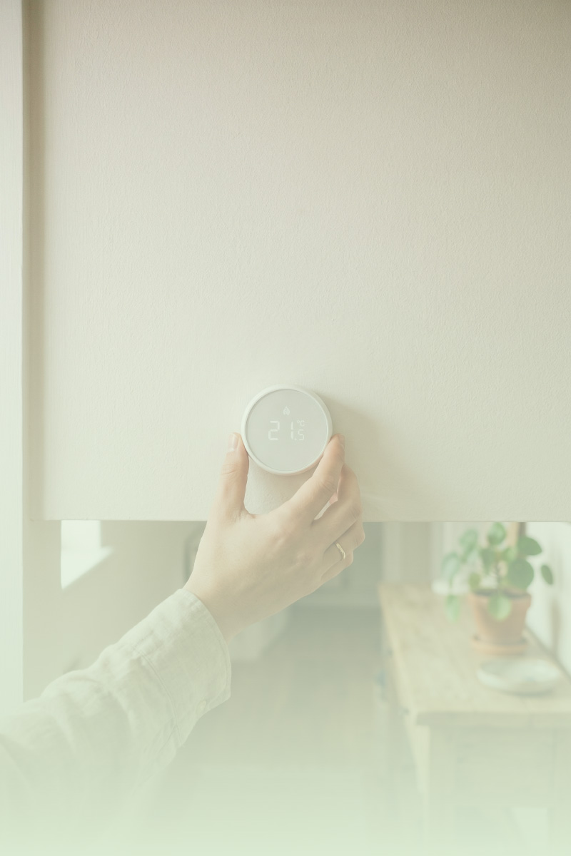 Hand adjusting a smart thermostat on a clean white wall